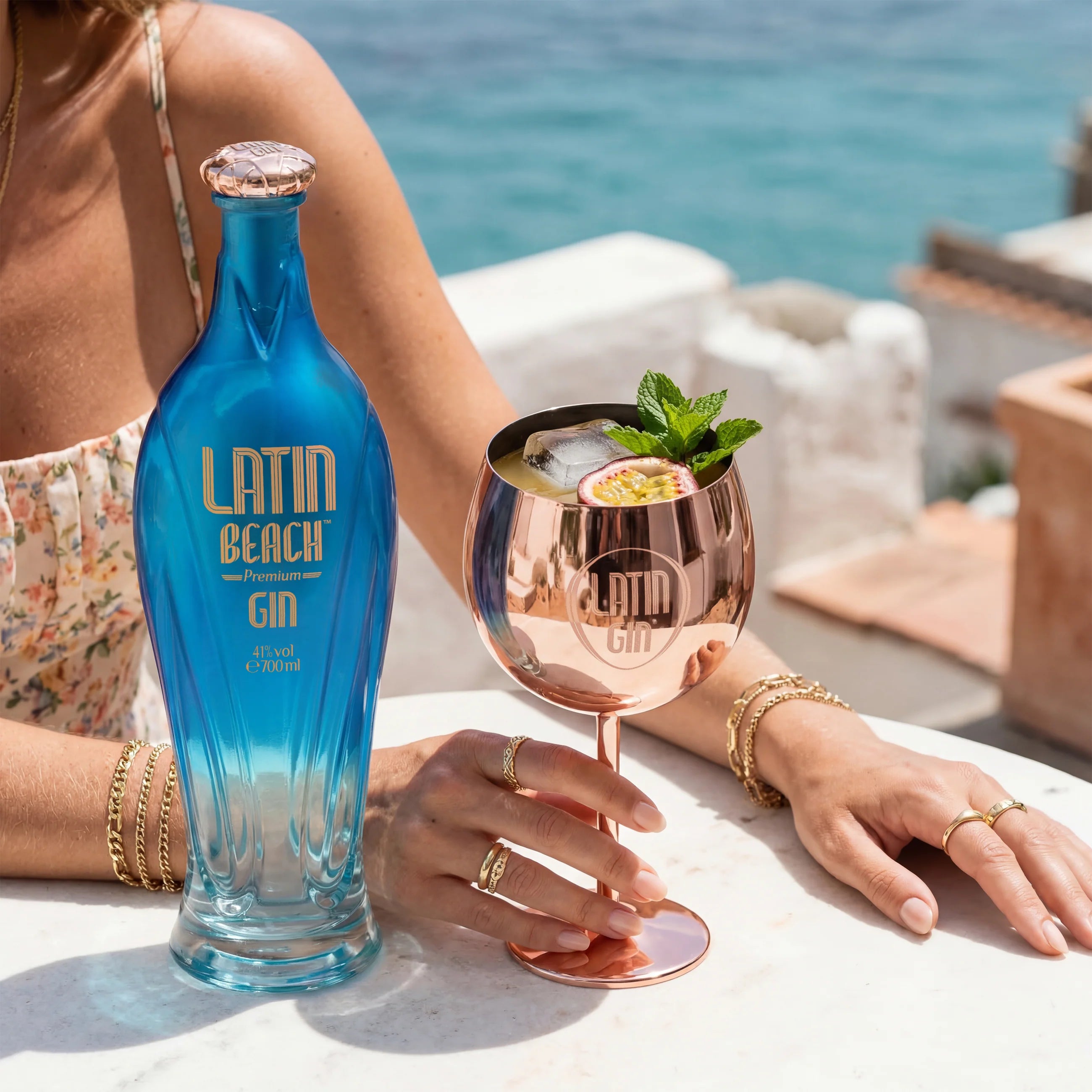 Load image into Gallery viewer, A woman enjoying a cocktail which is standing next to a bottle of Latin Beach Gin with a scenic Amalfi Coast background