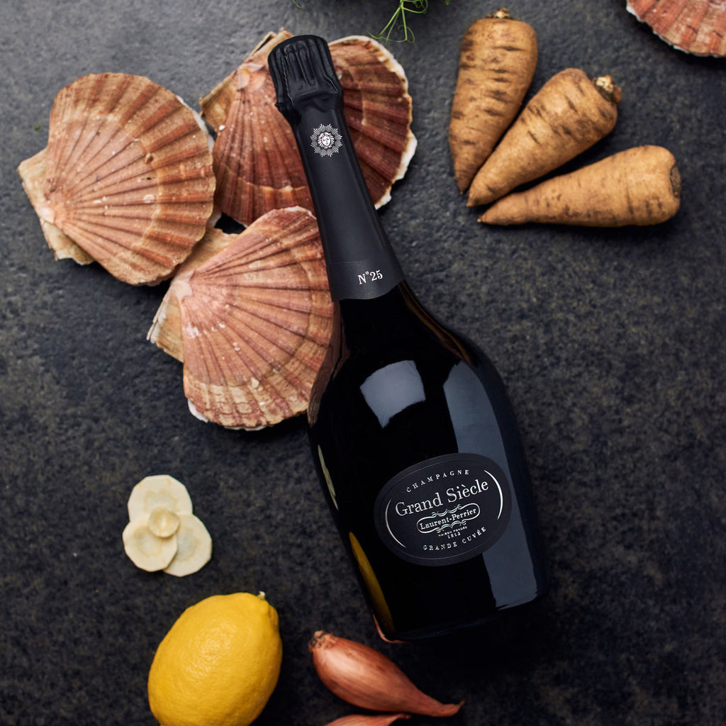 Bottle of Grand Siecle champagne with scallop shells, lemon, and parsnips on a dark surface