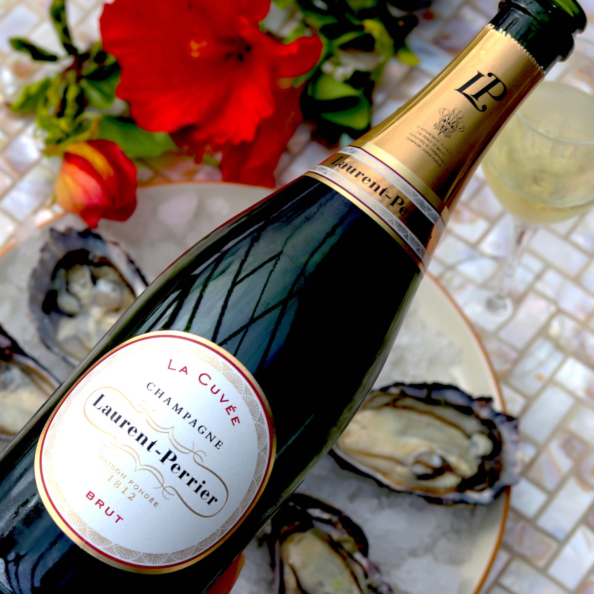Load image into Gallery viewer, A bottle of Laurent-Perrier La Cuvée Brut Champagne and oysters on a table with red flowers on it