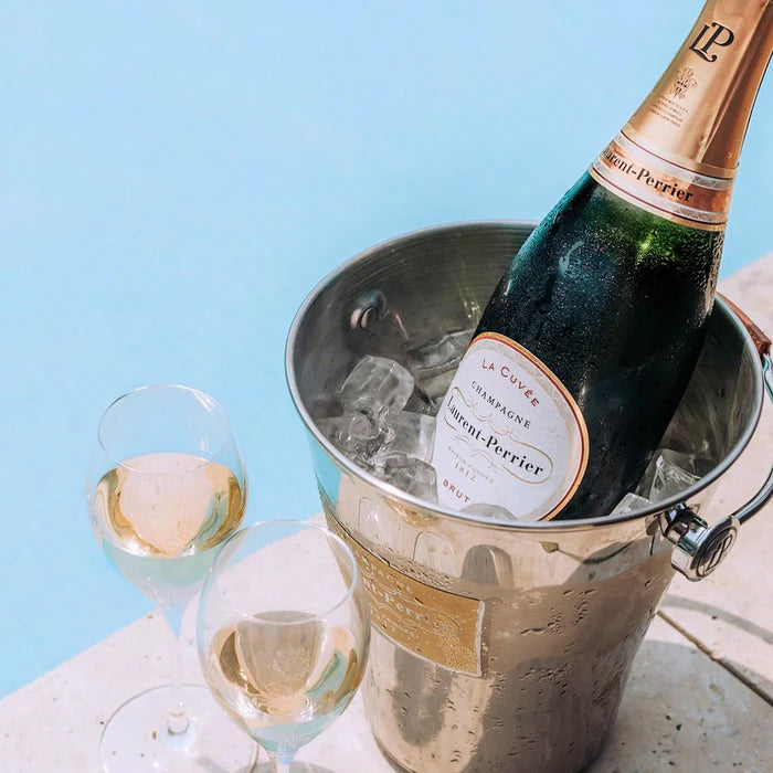 Bottle of Laurent-Perrier champagne in an ice bucket with two glasses on a light blue background