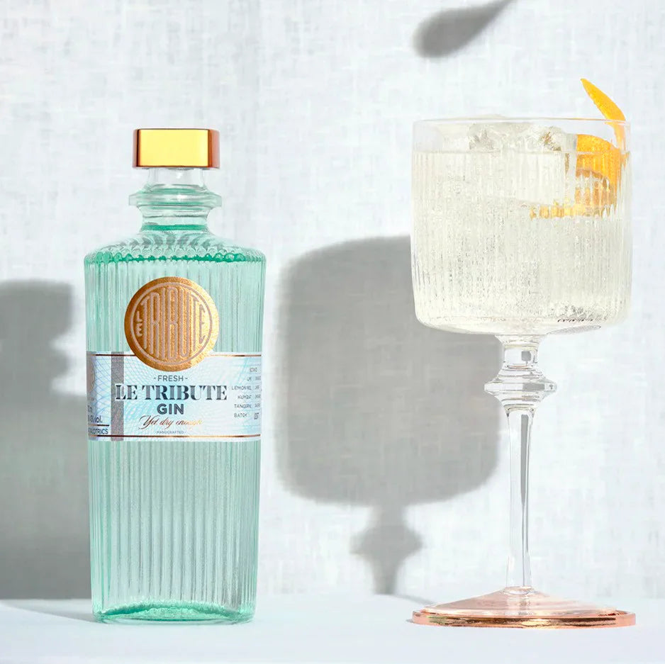 Bottle of Le Tribute Gin with a cocktail garnished with a lemon twist on a light background