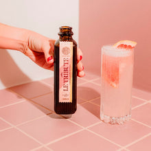 Load image into Gallery viewer, Bottle of Le Tribute Pink Grapefruit Tonic Water  with a cocktail on a pink tiled surface, featuring awards text.