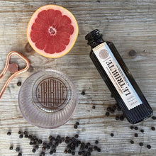 Load image into Gallery viewer, Bottle of Le Tribute Tonic Water, half a grapefruit, glass, and peppercorns on a wooden surface