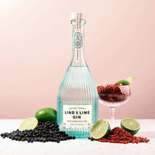 Load image into Gallery viewer, Bottle of Lind &amp; Lime Gin with limes, blackberries, and a glass on a pink background