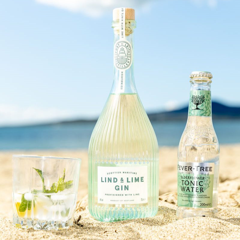 Load image into Gallery viewer, Bottle of Lind &amp; Lime Gin and Fever-Tree Tonic Water on a beach with ocean view.