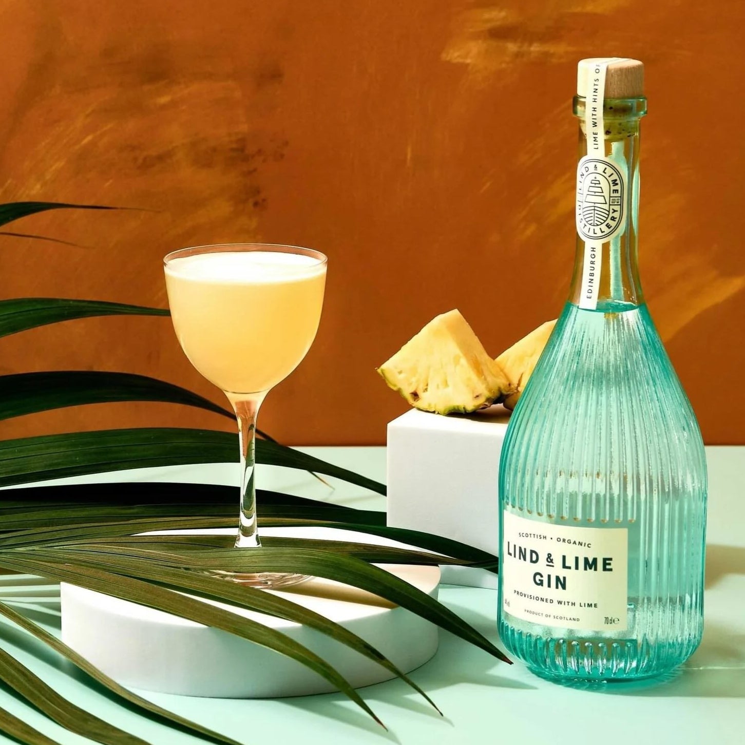 Load image into Gallery viewer, Bottle of Lind &amp; Lime gin with a cocktail and pineapple on a table against an orange wall.