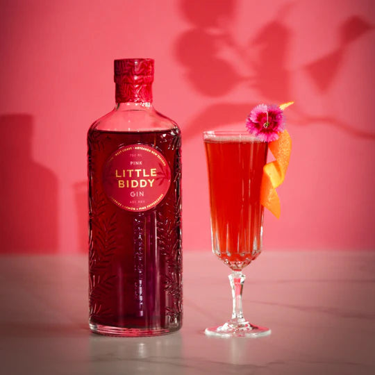 Bottle of Little Biddy Gin with a cocktail garnished with a flower on a pink background