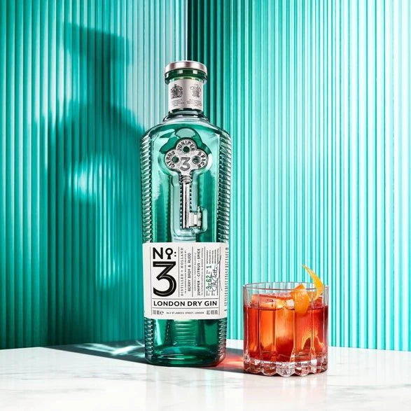 Load image into Gallery viewer, A bottle of gin and a cocktail on a marble table with a green background.