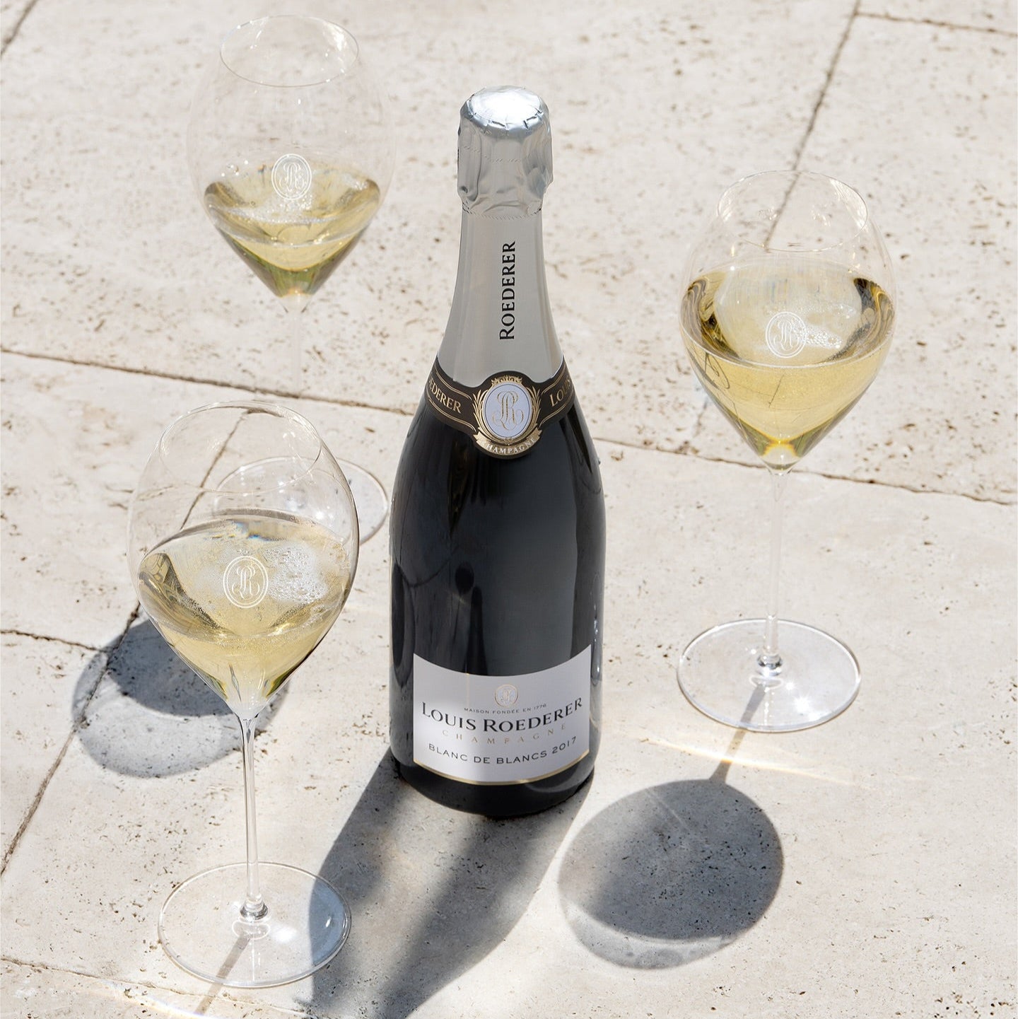 Load image into Gallery viewer, Bottle of Louis Roederer champagne with three glasses on a stone surface