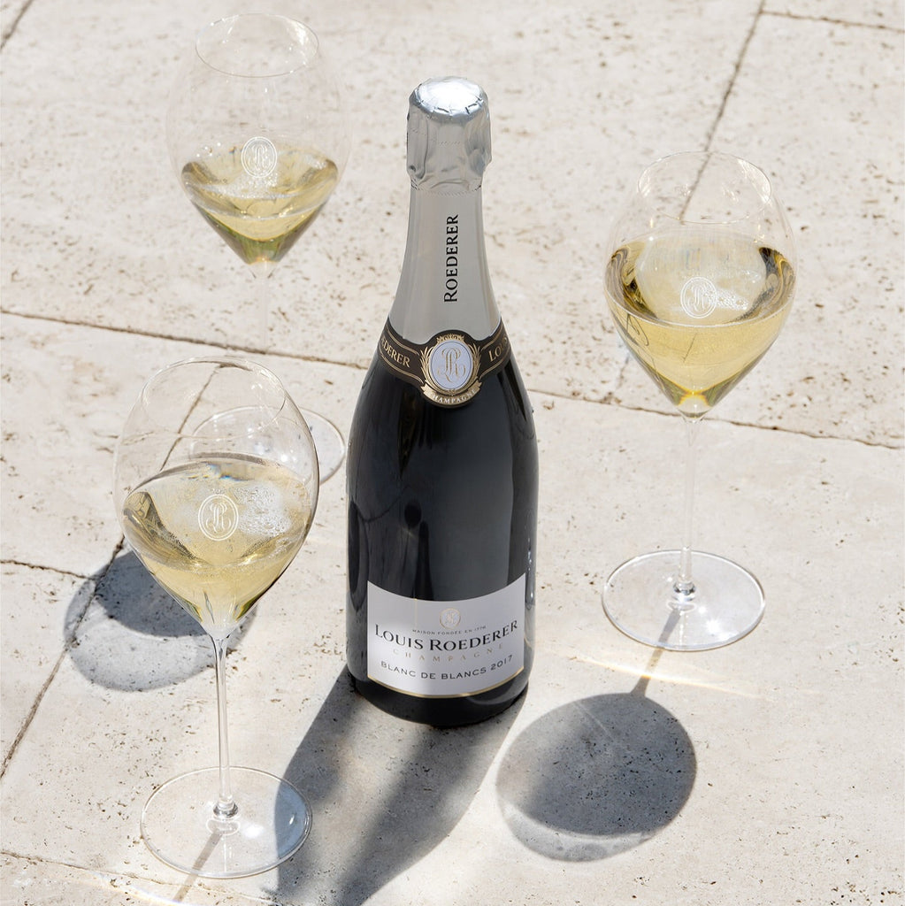 Bottle of Louis Roederer champagne with three glasses on a stone surface