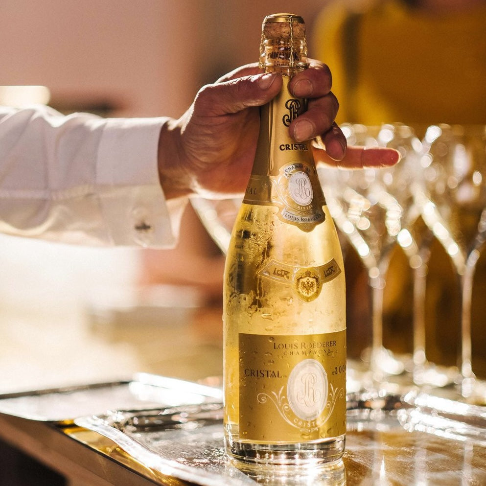 Load image into Gallery viewer, A hand holding on to a bottle of Louis Roederer Cristal Champagne in a bar