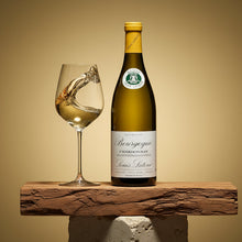 Load image into Gallery viewer, Bottle of Louis Latour Bourgogne Chardonnay wine with a glass of wine on a wooden surface against a beige background