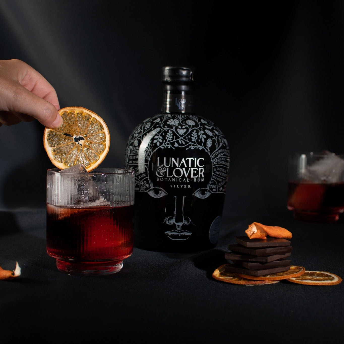 Load image into Gallery viewer, Bottle of 'Lunatic Lover' silver rum with a cocktail and garnish on a dark background