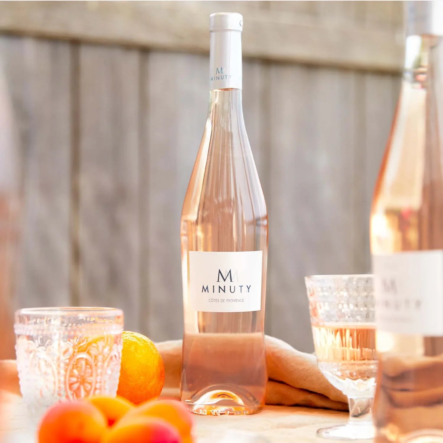 Load image into Gallery viewer, A bottle of rose wine and glasses on a table with some citrus fruit.