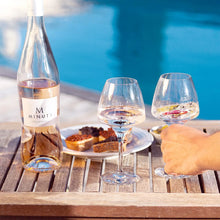 Load image into Gallery viewer, A bottle of M de Minuty Provence Rosé on outdoor wooden table next to two wines glasses and a pool in the background