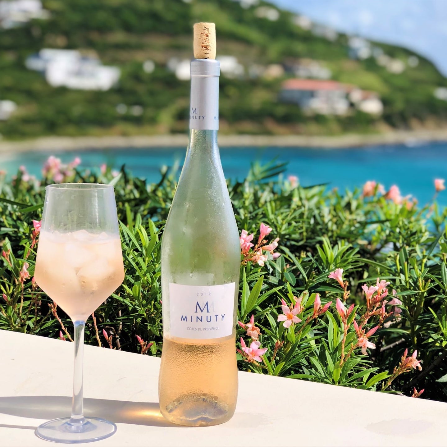 Load image into Gallery viewer, Bottles of M de Minuty Provence Rosé on a table with a wine glass with a seaside background 