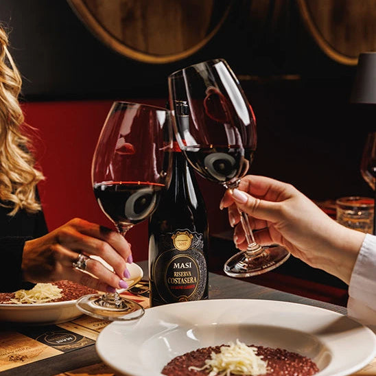 Two people enjoying a meal with a bottle of MASI Amarone Riserva di Costasera Classico red wine in a restaurant setting.