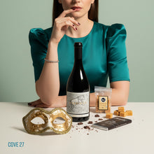 Load image into Gallery viewer, Woman in teal dress with a bottle of MITOLO MARSICAN SHIRAZ red wine bottle, packet of handcrafted 36 Degrees Vanilla fudge and Bennetts Dark chocolate bar, and mask on a light surface.