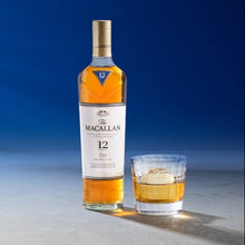 Load image into Gallery viewer, The Macallan 12 year old whiskey bottle with a glass of whisky on a gradient blue and gray background