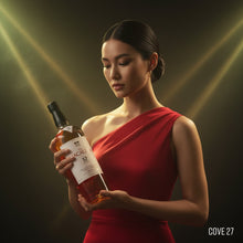 Load image into Gallery viewer, Woman in a red dress holding a bottle of Macallan 12 year old whisky against a dark background