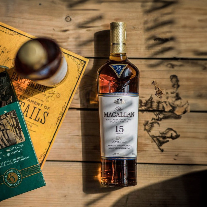 Bottle of The Macallan 15 year old whisky on a wooden surface with a menu and glasses.