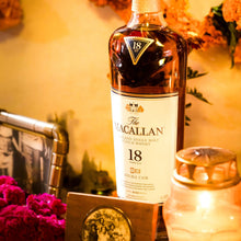 Load image into Gallery viewer, Macallan 18-year-old whisky bottle with decorative flowers and a glass in the background