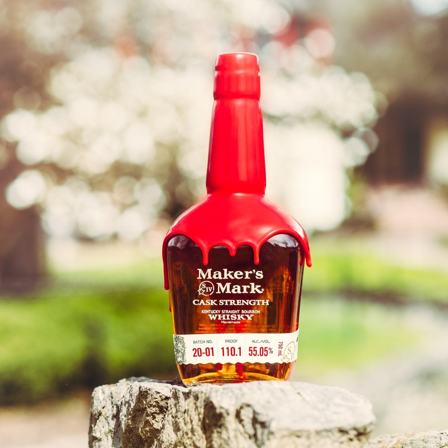 Load image into Gallery viewer, Makers Mark whiskey bottle on a stone surface with a blurred outdoor background