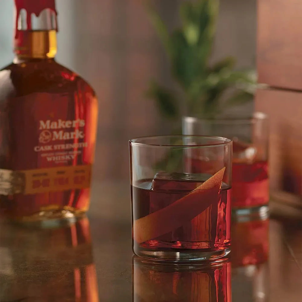 Load image into Gallery viewer, Makers Mark whiskey bottle with a glass of red liquid on a reflective surface.