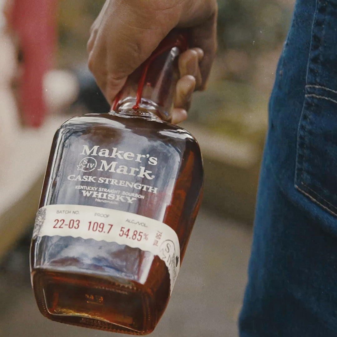 Load image into Gallery viewer, Hand holding a bottle of Maker's Mark Cask Strength Whiskey with a blurred background