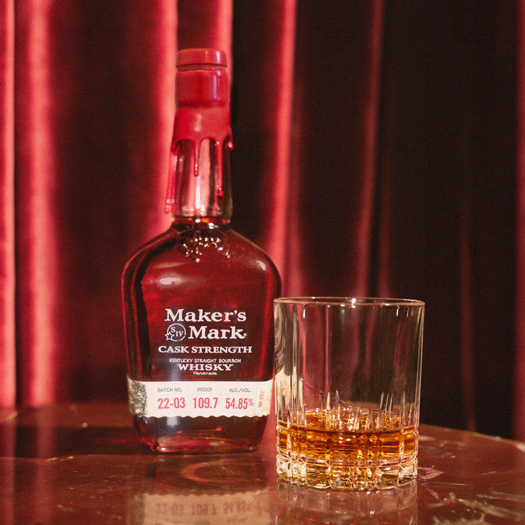 Load image into Gallery viewer, Maker's Mark Cask Strength whiskey bottle with a glass of whiskey on a reflective surface with red curtains in the background