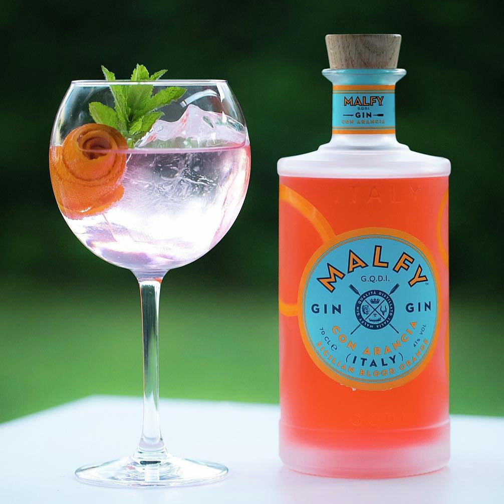 Load image into Gallery viewer, Bottle of Malfy Arancia Orange gin with a cocktail in a glass on a table.
