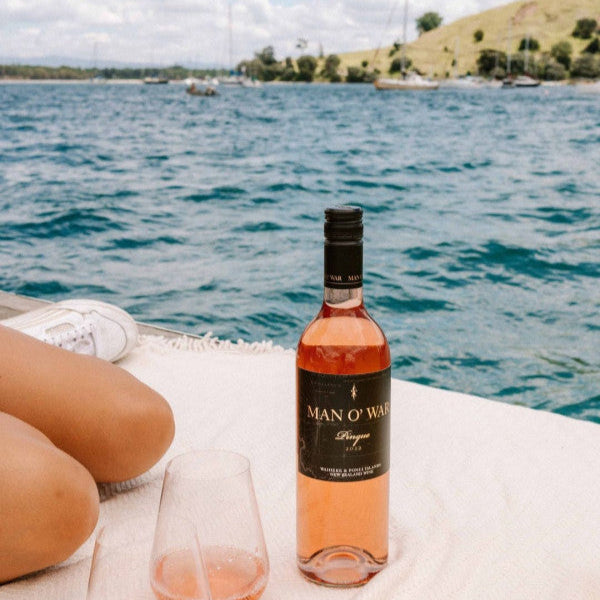 Load image into Gallery viewer, Bottle of Man O' War Rosé wine with a glass on a boat with a scenic background
