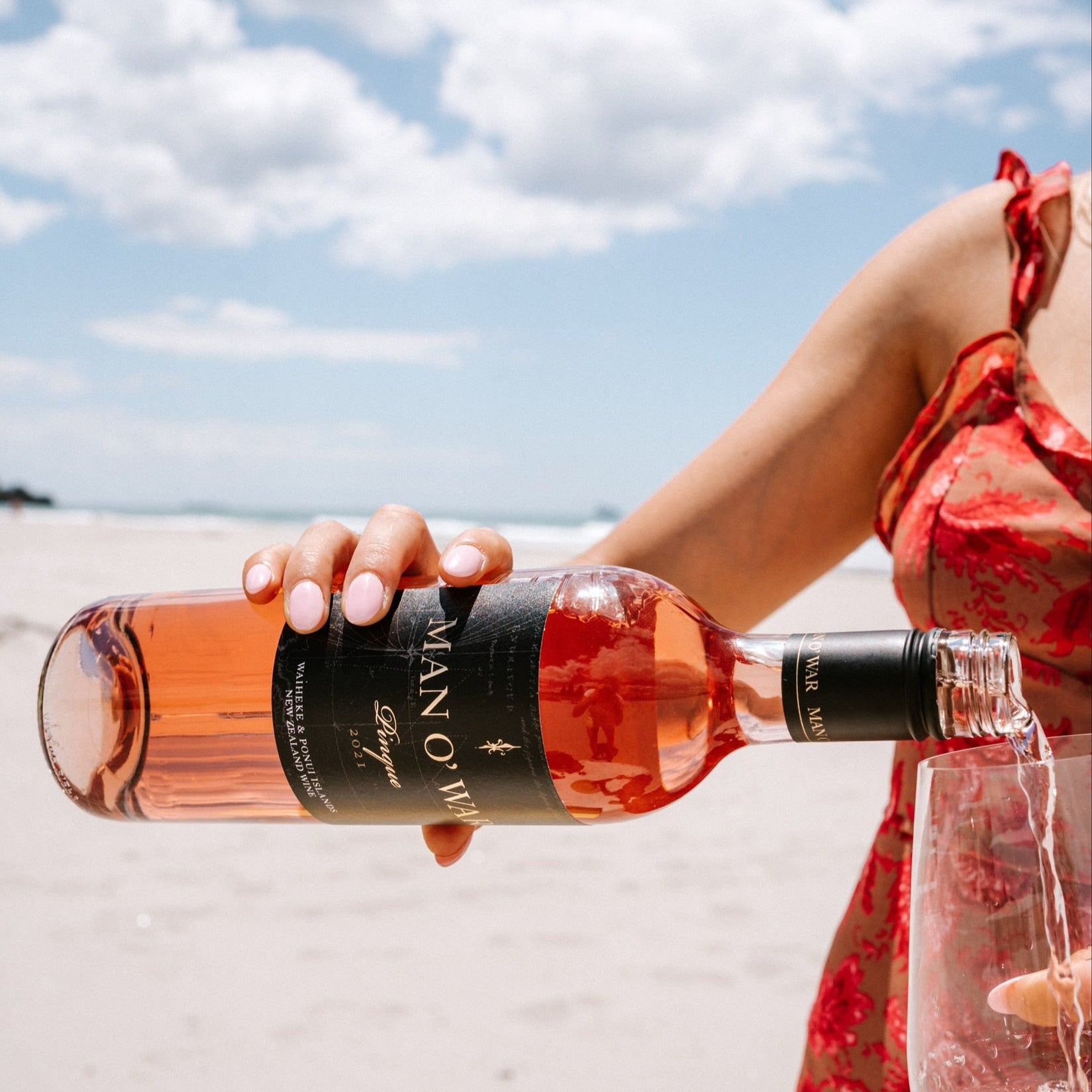 Load image into Gallery viewer, Person holding a bottle of rose wine on a beach with a clear sky.