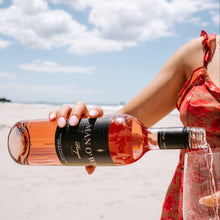 Load image into Gallery viewer, Person holding a bottle of rose wine on a beach with a clear sky.