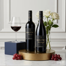 Load image into Gallery viewer, Two bottles of Man o' War wine on a wooden stand with a glass, grapes, and flowers in the background.