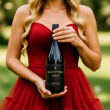 Load image into Gallery viewer, A blond woman in a red dress holding a bottle of Man O&#39; War Valhalla Chardonnay white wine in front of her.