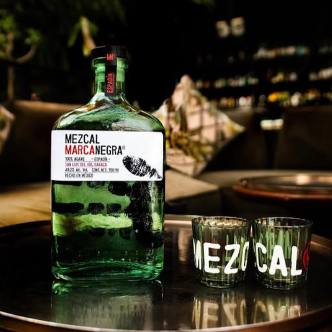Load image into Gallery viewer, Bottle of Mezcal Marca Negra with two glasses on a tray in a bar setting