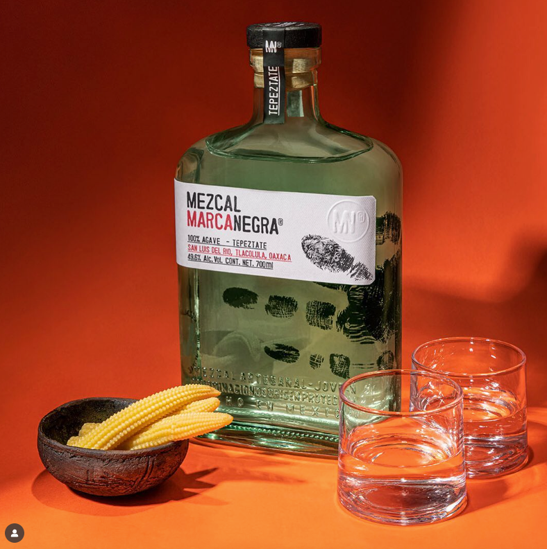 Load image into Gallery viewer, Mezcal Marcanegra bottle with corn and glasses on a red background