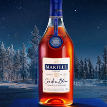 Load image into Gallery viewer, A bottle of Martell Cordon Bleu Cognac on a blue table with a wintery landscape as a background