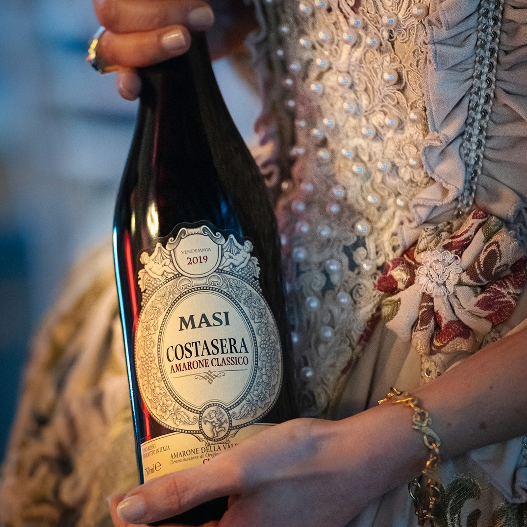 Load image into Gallery viewer, Woman holding a bottle of Masi Costasera Amarone Classico red wine, theatre dress