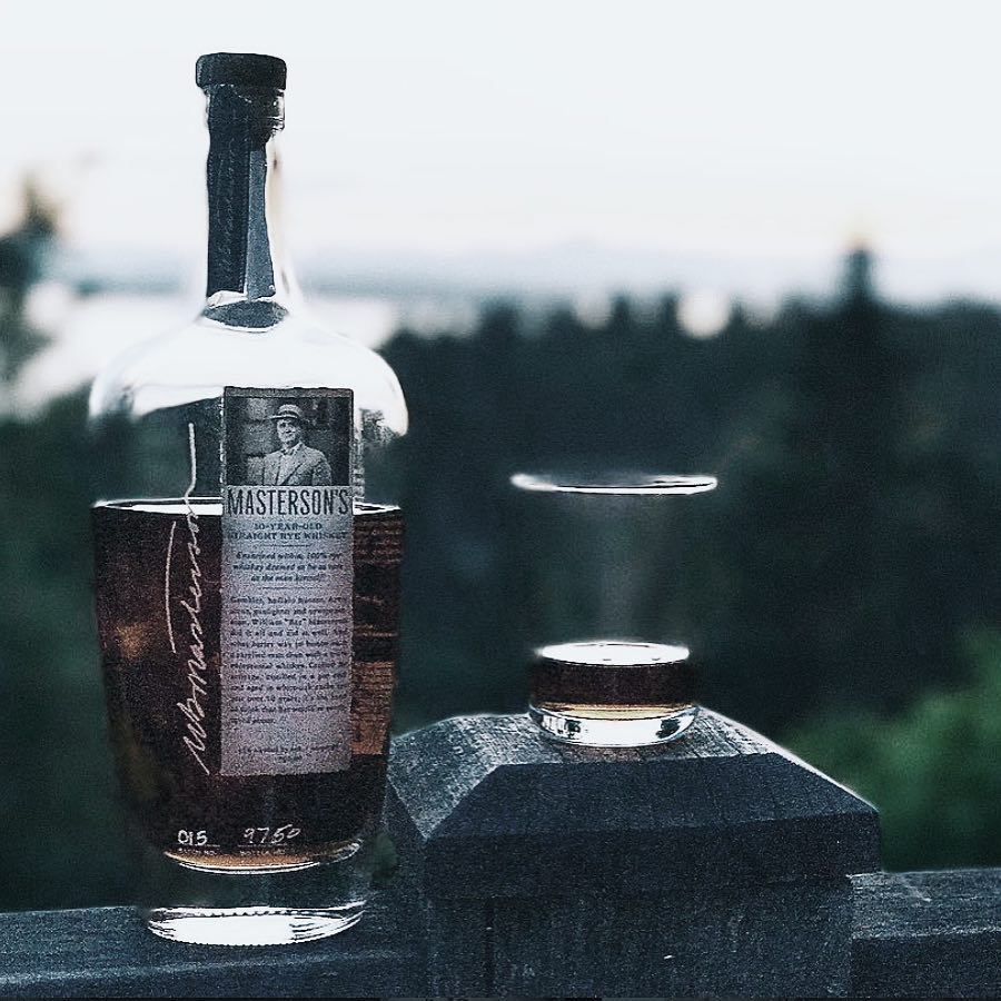 Load image into Gallery viewer, Bottle and glasses of Masterson's 10 Year Old Straight Rye whiskey on a stone surface with a blurred natural background