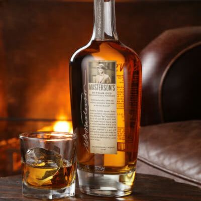 Load image into Gallery viewer, Bottle of Masterson's 10 Year Old Straight Rye whiskey with a glass on a wooden surface, fireplace in the background