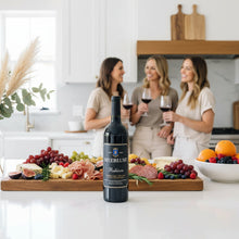 Load image into Gallery viewer, Three women in a kitchen enjoying a bottle of Meerlust Estate Rubicon red wine with a spread of food and a bottle of Merelussi wine.
