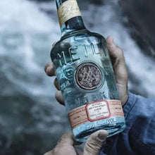 Load image into Gallery viewer, Hand holding a bottle of Meilli Vodka with a blurred natural background