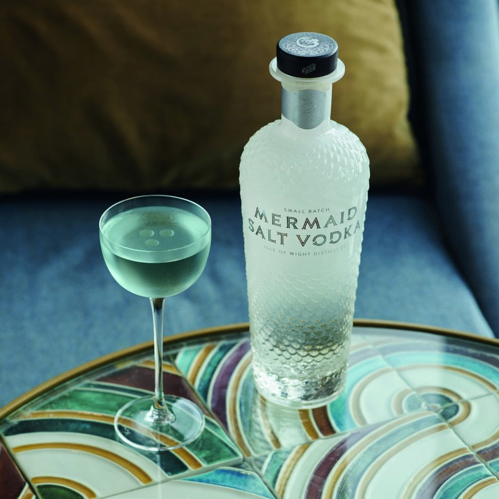 Mermaid Salt Vodka bottle with a glass of green liquid on a decorative table.