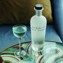 Load image into Gallery viewer, Mermaid Salt Vodka bottle with a glass of green liquid on a decorative table.