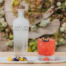 Load image into Gallery viewer, Mermaid Salt Vodka bottle with a cocktail on a table against a decorative background