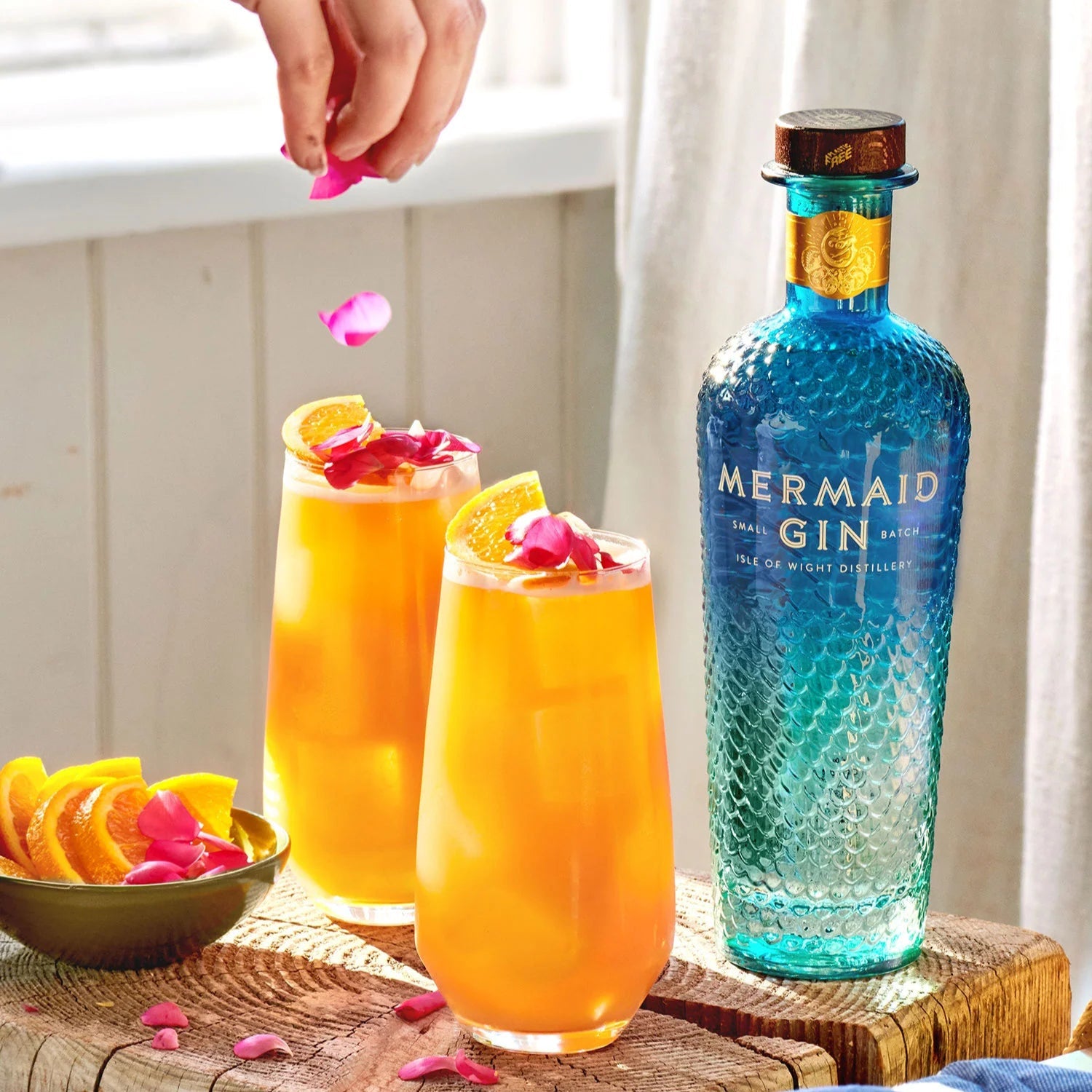 Load image into Gallery viewer, Mermaid Gin bottle with two cocktails garnished with flowers on a wooden surface.