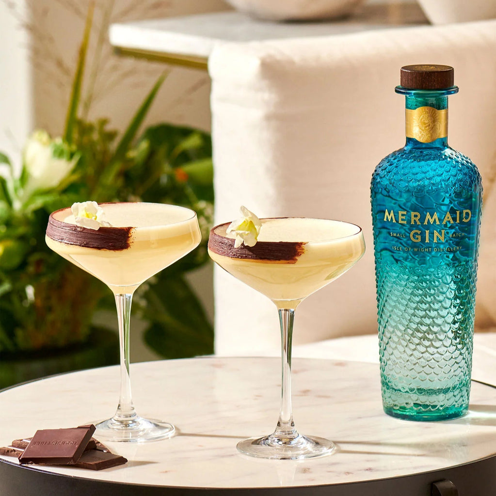 Mermaid Gin bottle with two cocktails on a table outdoors