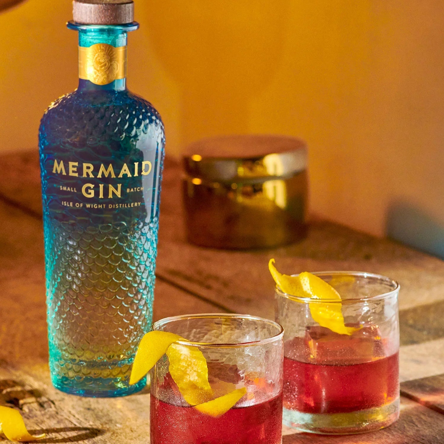 Load image into Gallery viewer, Mermaid Gin bottle with two glasses of red cocktails on a wooden surface.